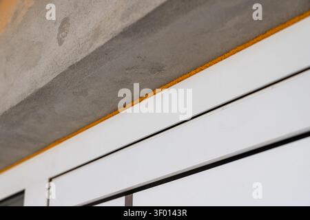 Detailed view of construction materials showing a rough concrete surface above a bright yellow sealant strip and a clean white window frame Stock Photo