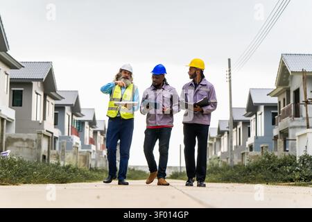 Construction engineers walking through residential development site to inspect and coordinate building progress, discussing work progress while walkin Stock Photo