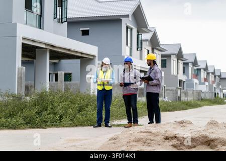 Construction engineers walking through residential development site to inspect and coordinate building progress, discussing work progress while walkin Stock Photo
