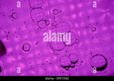 Vibrant abstract background of purple liquid with floating bubbles and tiny droplets, creating a glossy macro texture with soft bokeh light spots and Stock Photo