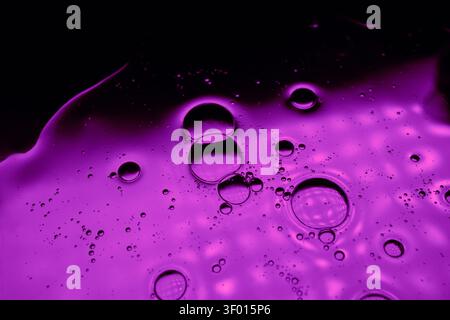 Vivid macro of purple liquid with floating oil bubbles and tiny droplets on a dark background, creating a glossy abstract texture for modern design an Stock Photo