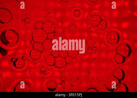 Vivid abstract macro of red liquid with clustered bubbles and tiny droplets, creating a glossy textured background ideal for science, cosmetic, or ene Stock Photo