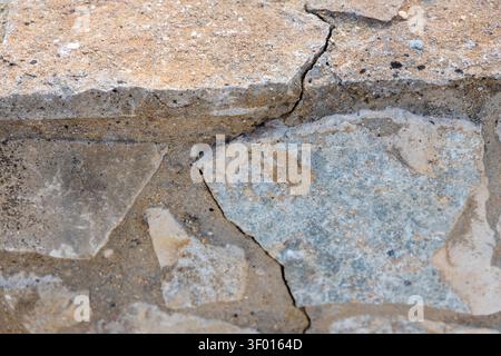 Detailed view of weathered stone blocks forming a wall, showcasing natural textures, cracks, and the granular composition of the surrounding mortar Stock Photo