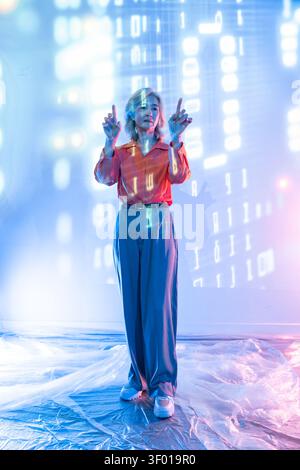 Futuristic senior Asian woman standing in neon light, interacting with a holographic data interface and digital code, showcasing innovation, AI techno Stock Photo