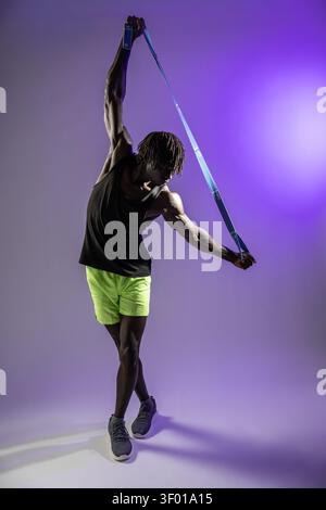 Full-length studio photo of a black male athlete stretching with a resistance band overhead, showing strength, flexibility, and warmup routine against Stock Photo