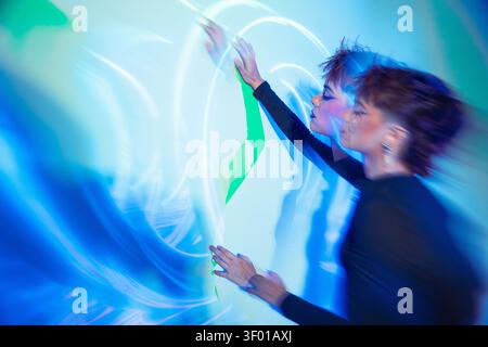 Cyberpunk young woman reaches toward a glowing hologram wall, bathed in blue and green neon light with motion blur, evoking futuristic tech, VR, and d Stock Photo