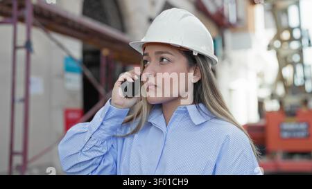 Woman engineer in white hardhat speaking into handheld radio while inspecting scaffolding at building construction site; professional focus. Stock Photo