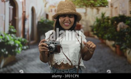 Woman adjusts vintage camera strap on a cobblestone street while squinting at the viewfinder; travel exploration frustration. Stock Photo
