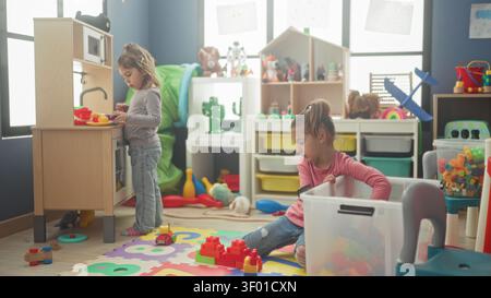 Girl plays with colorful blocks and toy kitchen using hands while kneeling on foam mat in a bright indoor playroom; quiet concentration. Stock Photo