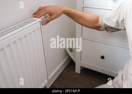 Closeup of male hand adjusting thermostat on white radiator. Home heating control, energy saving and utility cost management concept. Person Stock Photo
