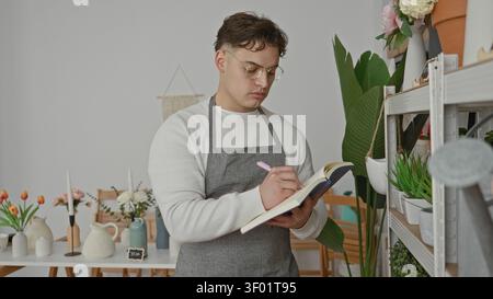 Man florist writes in notebook with hand holding pink pen beside potted plants in studio; quiet focus. Stock Photo