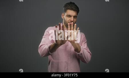 Man with beard holds both hands up in stop gesture and shields face wearing pink shirt in studio; defensive. Stock Photo