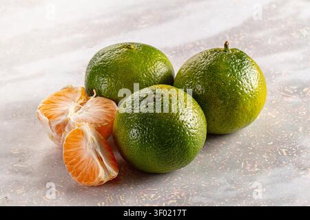 Fresh green tangerines arranged on marbled surface with one peeled segment showing juicy orange flesh. Soft lighting highlights texture vibrant colors Stock Photo