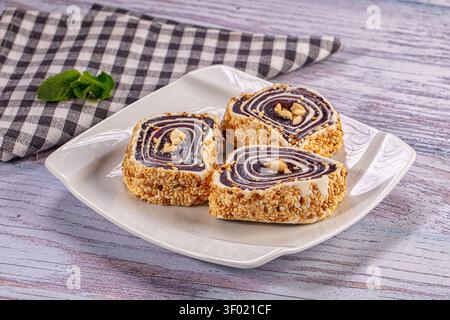 Sliced sweet rolls with chocolate swirl sesame seed coating on white plate. Rustic wooden background with checkered napkin mint leaf. Warm lighting hi Stock Photo