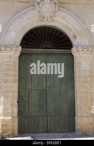 Ancient stone archway with decorative carvings and an oval crest, framing a tall, closed, weathered green wooden door. Italy, lecce, 18 july 2025 Stock Photo
