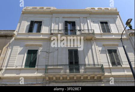 Classic architectural building facade featuring multiple windows with closed wooden shutters and ornate wrought iron balconies under a clear sky. Ital Stock Photo