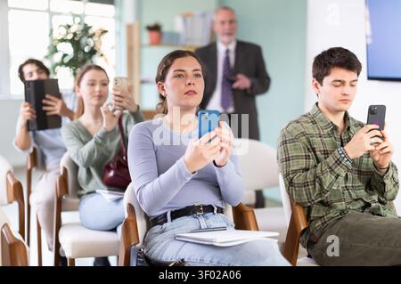 Young female student scans QR code or takes photo, teacher in background Stock Photo