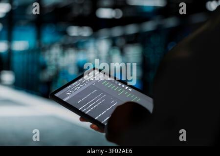 Data center engineer uses a digital tablet in a data center to troubleshoot backend operations and resolve system crashes. Stock Photo