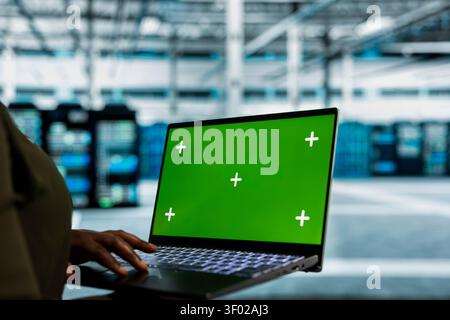 Data center administrator works with a chroma key laptop, using an editable screen to review performance data. Stock Photo