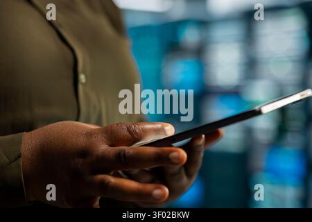 Data center engineer uses a digital device in a data center to monitor equipment, manage workflows, and support reliable infrastructure. Stock Photo