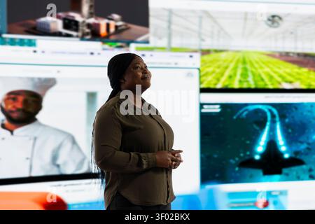 Cheerful woman looking at video wall, enjoying endless entertainment selection. Happy person satisfied by access to various streaming options, looking at screens displaying movies and TV shows. Stock Photo