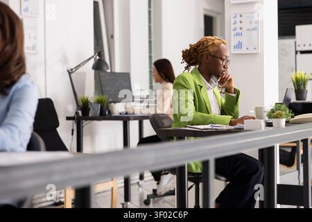 Skilled business advisor works at office desk, analyzing information on digital device and preparing reports. African american woman seated with focus, checking marketing strategy for presentations. Stock Photo