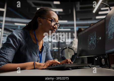 Focused server facility engineer applying AI ML tech. African American woman in server facility looking at AI programming tools on workstation check to update equipment. Stock Photo