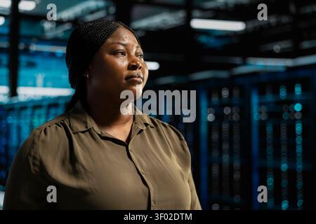 System admin walking in computing facility with server hardware supporting business needs, while doing checkup, ensuring equipment works at optimum operational performance for smooth operations. Stock Photo