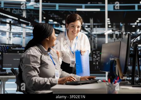 Smiling data center team works with digital devices while reviewing systems, scripts and server infrastructure. Stock Photo