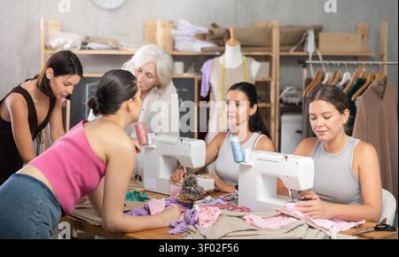 Older and younger women sewing and chatting in workroom Stock Photo