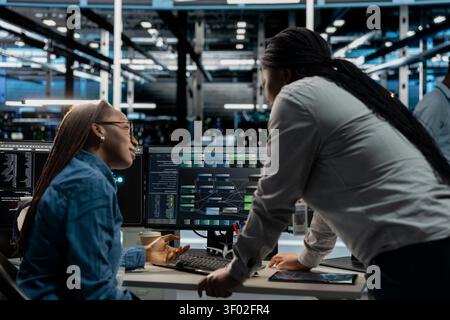 Server facility supervisor supervising technical work from systems engineer applying AI neural network models. Stock Photo