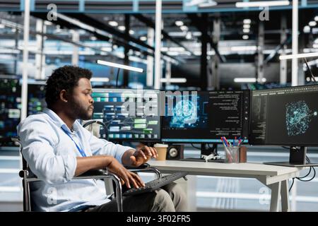 Data center engineer using a wheelchair uses a computer to manage machine learning workloads, working with AI technology and high performance systems. Stock Photo