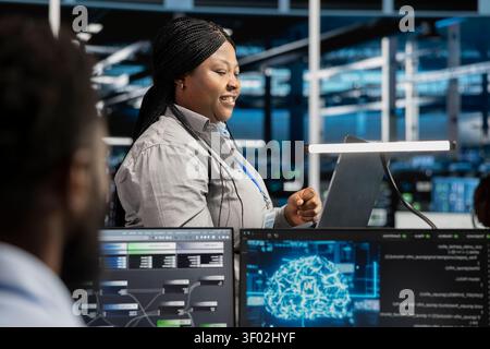 Cheerful data center engineer applying AI to enhance operational efficiency and reduce downtime. Happy staff member designs and implements AI driven solutions for server facility equipment. Stock Photo