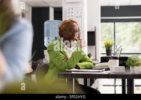 Corporate worker sitting deep in thought, considering creative ways to achieve company marketing targets. Pensive professional woman with finger on mouth, thinking on potential business projects. Stock Photo