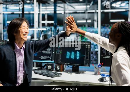 Delighted data center colleagues share a high five after improving system efficiency and completing AI implementation. Stock Photo