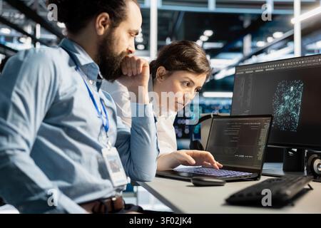 Data center colleagues collaborate on coding and AI automation scripts while reviewing server infrastructure together. Stock Photo