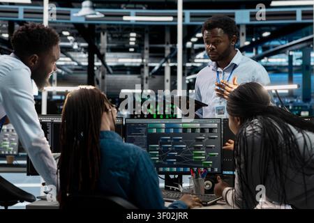 Engineers brainstorm and program inside a server farm, using a PC to repair data center racks and manage computational operations. Stock Photo