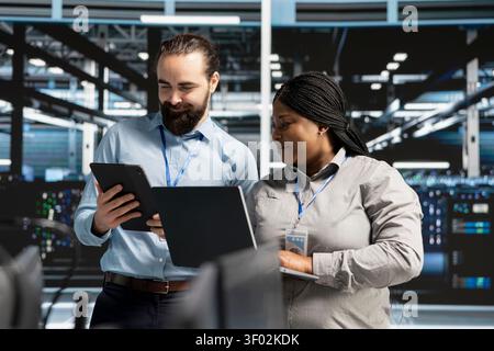 Smiling data center team works with digital devices while reviewing systems, scripts and server infrastructure. Stock Photo