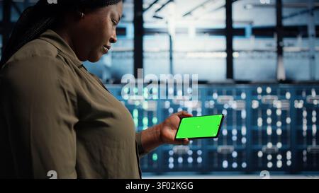 Data center administrator works with a chroma key smartphone, using an editable screen to watch a technical tutorial. Stock Photo