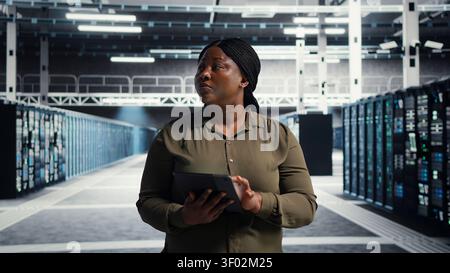 Technical specialist working with digital tablet in server facility, integrating new technologies and systems. Stock Photo