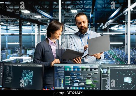 Engineers coding in data infrastructure center, updating AI driven automation scripts, while IT staff members working in server facility programming AI algorithms, debugging equipment. Stock Photo