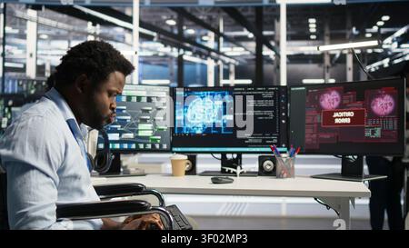 Stressed technical specialist with paraplegia in computing facility panicked by AI visual programming system urgent system alert with anxious computing hub staff member in wheelchair worried. Stock Photo