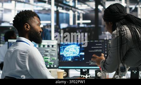 Server room supervisor overseeing work done by engineer working with deep learning models to review data sets. Stock Photo