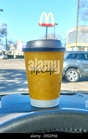 DALLAS, TX, USA - FEBRUARY 16, 2024: A McCafé coffee cup is prominently placed on a car dashboard in front of a McDonald's restaurant. The yellow cup, Stock Photo