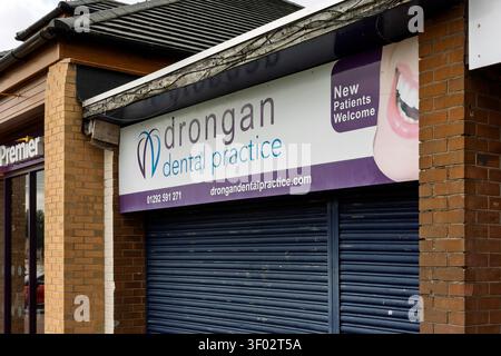 Drongan, UK - May 24, 2025: The exterior sign of Drongan Dental Practice, a "New Patients Welcome" NHS dental surgery, above a closed blue roller shut Stock Photo