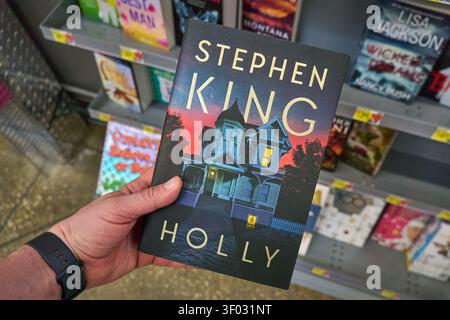 CARROLLTON, TX, USA - FEBRUARY 24, 2024: A person holds up Stephen King's novel 'Holly' inside a bookstore. The cover illustration showcases a house a Stock Photo