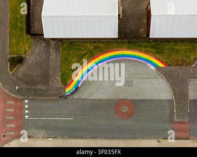 Aerial view of a vibrant rainbow-painted curb bordering a paved area next to a building with white roofs and road markings in Iceland. Stock Photo
