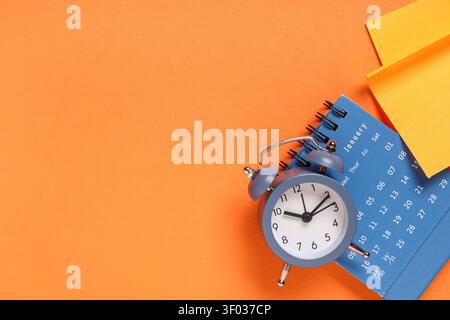 Calendar with alarm clock and sticky notes on orange background Stock Photo