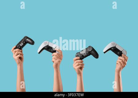 Hands holding black and white video game controllers on blue background Stock Photo