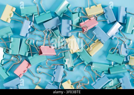 Close-up of pastel binder clips scattered on a blue surface, suitable for office organization, school supplies, paperwork, planning, creativity, and w Stock Photo
